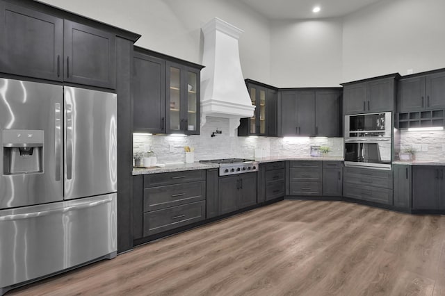 2172 Greentree Dr, Huntsville, TX 77340 - kitchen with stainless steel appliances, custom exhaust hood, light stone counters, glass insert cabinets, and light wood finished floors