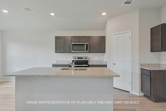 217 Rockbridge Dr, Huntsville, TX 77340 - kitchen featuring appliances with stainless steel finishes, dark brown cabinets, light wood-style floors, light stone counters, and recessed lighting