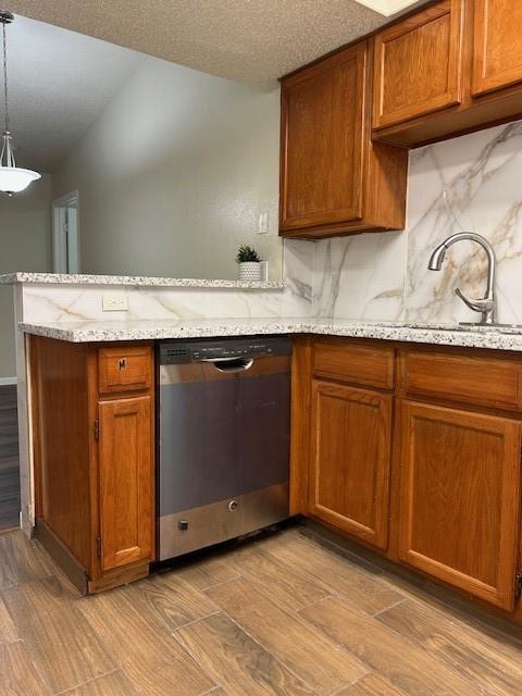 10555 Turtlewood Ct Unit 2111, Houston, TX 77072 - kitchen featuring stainless steel dishwasher, light wood-style flooring, a peninsula, brown cabinets, and a textured ceiling