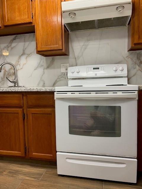 10555 Turtlewood Ct Unit 2111, Houston, TX 77072 - kitchen featuring white range with electric stovetop, under cabinet range hood, decorative backsplash, and brown cabinets