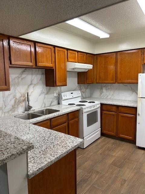 10555 Turtlewood Ct Unit 2111, Houston, TX 77072 - kitchen with white appliances, under cabinet range hood, a peninsula, brown cabinetry, and backsplash
