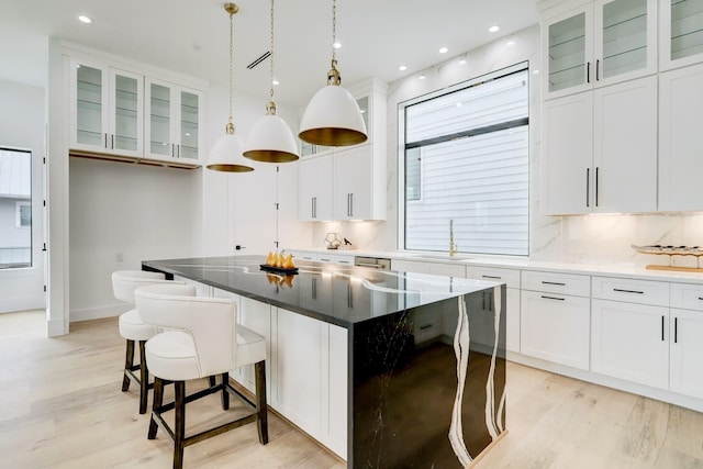 1022 Allston St, Houston, TX 77008 - kitchen featuring light wood-style floors, white cabinets, a kitchen island, a kitchen bar, and glass insert cabinets
