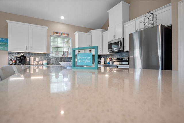 975 S S Cv, Crystal Beach, TX 77650 - kitchen with appliances with stainless steel finishes, decorative backsplash, white cabinets, light stone counters, and vaulted ceiling