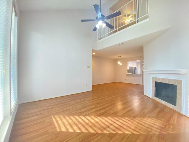 2601 S Braeswood Blvd Unit 605, Houston, TX 77025 - unfurnished living room with a tiled fireplace, light wood-style floors, ceiling fan, and a towering ceiling