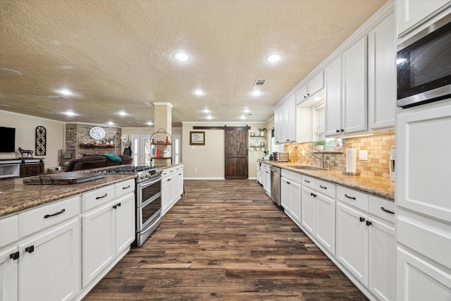 3214 Churchill St, Pearland, TX 77581 - kitchen featuring stainless steel appliances, a barn door, a textured ceiling, white cabinetry, and dark wood-type flooring