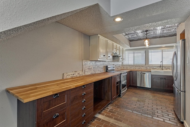 1437 Bowsprit Pt, Willis, TX 77318 - kitchen featuring stainless steel appliances, wood counters, brick floors, under cabinet range hood, and a textured wall