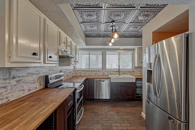 1437 Bowsprit Pt, Willis, TX 77318 - kitchen with stainless steel appliances, wood counters, under cabinet range hood, an ornate ceiling, and brick floors