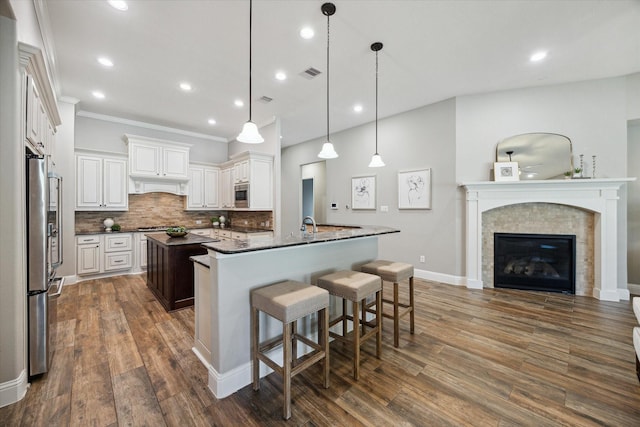 27722 Lakeway Trail Ln, Fulshear, TX 77441 - kitchen featuring an island with sink, freestanding refrigerator, backsplash, dark wood-style flooring, and a kitchen breakfast bar