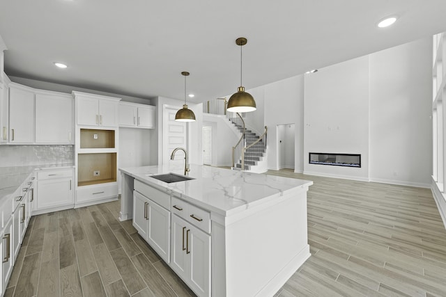 10922 Palmwood Dr, Missouri City, TX 77459 - kitchen featuring light wood-style flooring, an island with sink, light stone counters, white cabinets, and recessed lighting
