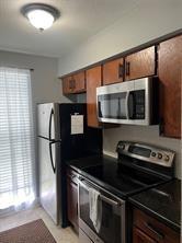 12500 Sandpiper Dr Unit 57, Houston, TX 77035 - kitchen featuring appliances with stainless steel finishes, dark countertops, plenty of natural light, and brown cabinets
