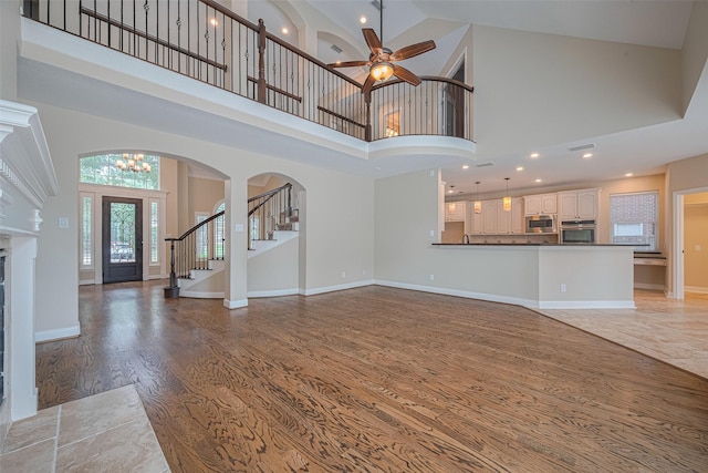 9 Foxworth Ct, Sugar Land, TX 77479 - unfurnished living room with a towering ceiling, light wood-type flooring, a ceiling fan, stairway, and a fireplace