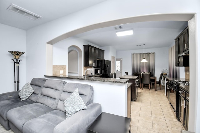 14710 Branchwest Dr, Houston, TX 77082 - kitchen featuring black appliances, dark stone countertops, light tile patterned flooring, arched walkways, and a kitchen breakfast bar