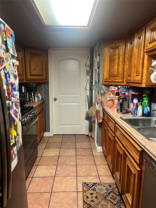 11733 Knotty Pine Trl, Houston, TX 77050 - kitchen featuring freestanding refrigerator, black range with gas cooktop, light tile patterned floors, dishwasher, and light countertops