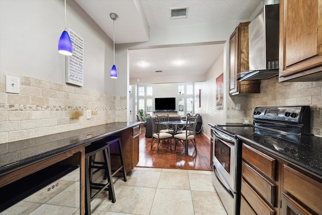 1018 Memorial Village Dr Unit 124, Houston, TX 77024 - kitchen with stainless steel electric stove, wall chimney range hood, tasteful backsplash, pendant lighting, and dark stone counters