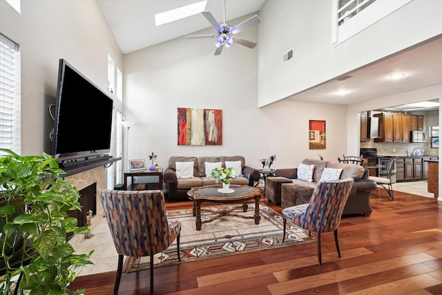 1018 Memorial Village Dr Unit 124, Houston, TX 77024 - living room with ceiling fan, high vaulted ceiling, light wood-style floors, a fireplace, and a skylight