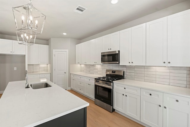 2845 14th St, Hempstead, TX 77445 - kitchen with appliances with stainless steel finishes, white cabinets, light wood-style flooring, a chandelier, and tasteful backsplash