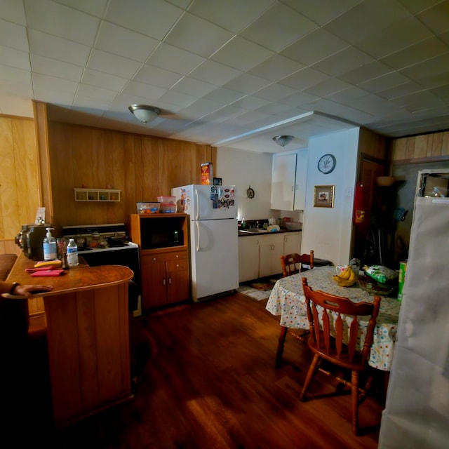 710 College St, El Campo, TX 77437 - kitchen with freestanding refrigerator, dark wood-type flooring, wood walls, and brown cabinetry