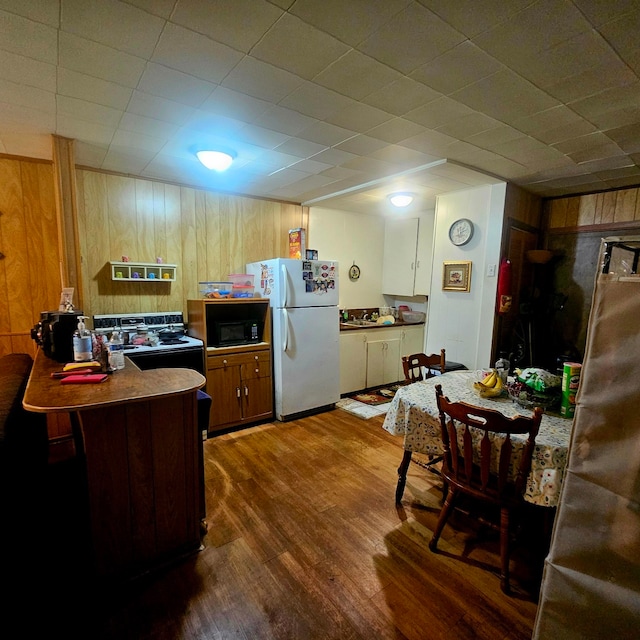 710 College St, El Campo, TX 77437 - kitchen with freestanding refrigerator, wooden walls, dark wood-style floors, range with electric cooktop, and a peninsula