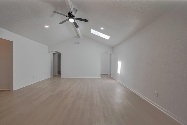 6219 Canada Dr, Pasadena, TX 77505 - unfurnished living room with arched walkways, a skylight, light wood-style flooring, ceiling fan, and a textured ceiling