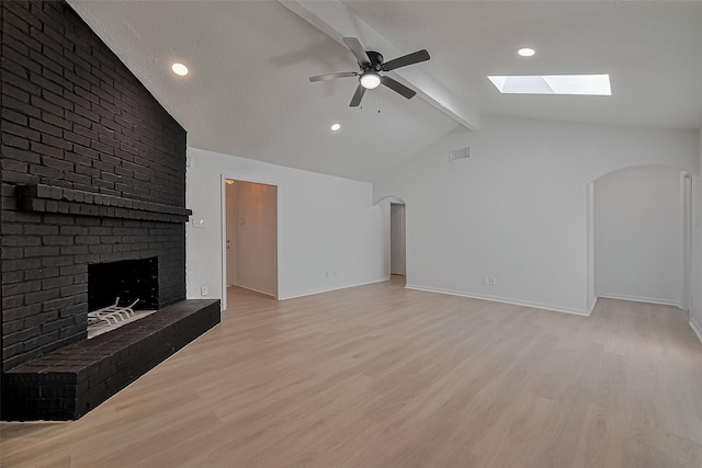 6219 Canada Dr, Pasadena, TX 77505 - unfurnished living room featuring arched walkways, a fireplace, ceiling fan, a skylight, and light wood finished floors