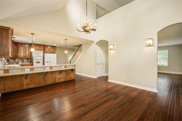 238 Horse Shoe Trl, Angleton, TX 77515 - kitchen featuring white appliances, arched walkways, brown cabinetry, a kitchen bar, and high vaulted ceiling
