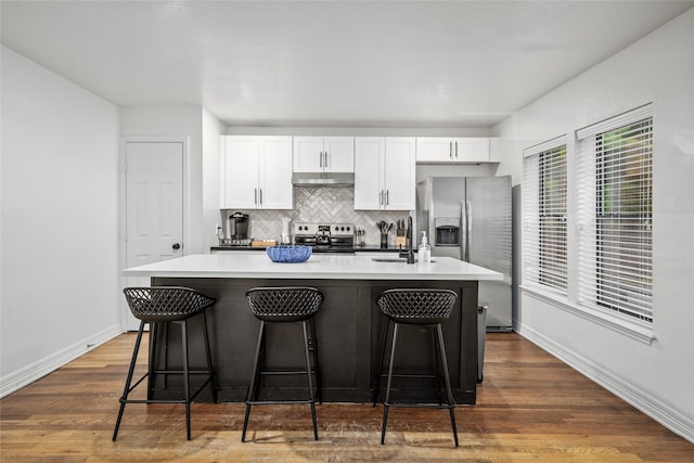 3404 Rosedale St, Houston, TX 77004 - kitchen with appliances with stainless steel finishes, under cabinet range hood, a center island with sink, white cabinetry, and decorative backsplash