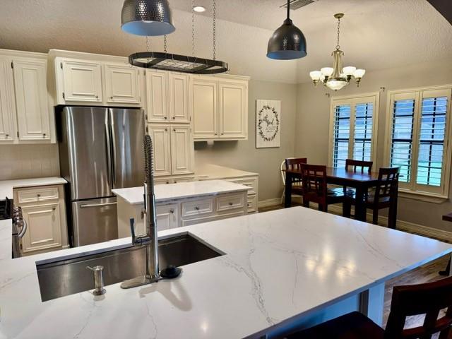 108 Audubon Woods Dr, Richwood, TX 77531 - kitchen with freestanding refrigerator, a chandelier, decorative light fixtures, white cabinetry, and light stone counters