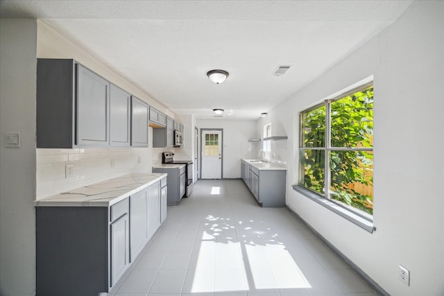 604 Briarclift Ln, Baytown, TX 77521 - kitchen featuring appliances with stainless steel finishes, gray cabinetry, light countertops, decorative backsplash, and light tile patterned flooring