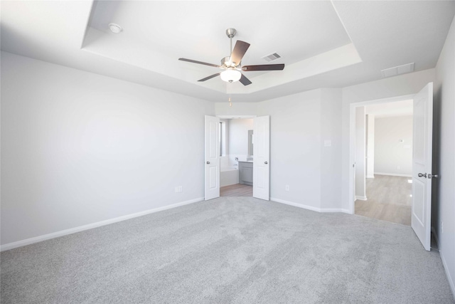 16866 Needlepoint Dr, Conroe, TX 77302 - unfurnished bedroom with a tray ceiling, light colored carpet, ceiling fan, and connected bathroom