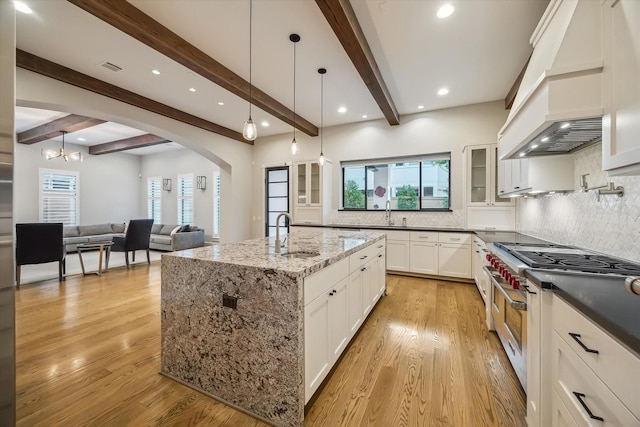 1116 W Drew St, Houston, TX 77006 - kitchen featuring range with two ovens, custom exhaust hood, beam ceiling, glass insert cabinets, and arched walkways