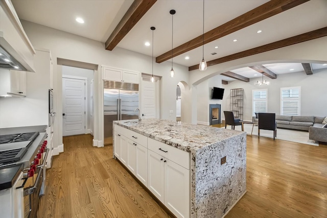 1116 W Drew St, Houston, TX 77006 - kitchen featuring arched walkways, wall chimney range hood, high end appliances, open floor plan, and light wood-style floors