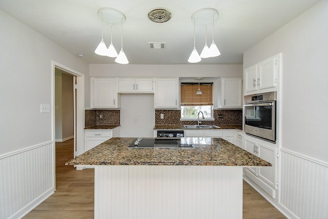 1010 Rock Canyon Dr, Katy, TX 77450 - kitchen with oven, black electric cooktop, white cabinetry, light wood-type flooring, and wainscoting