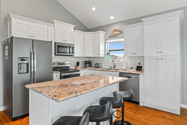 18607 Warrior Rd, Galveston, TX 77554 - kitchen with appliances with stainless steel finishes, light wood-style flooring, vaulted ceiling, white cabinets, and decorative backsplash