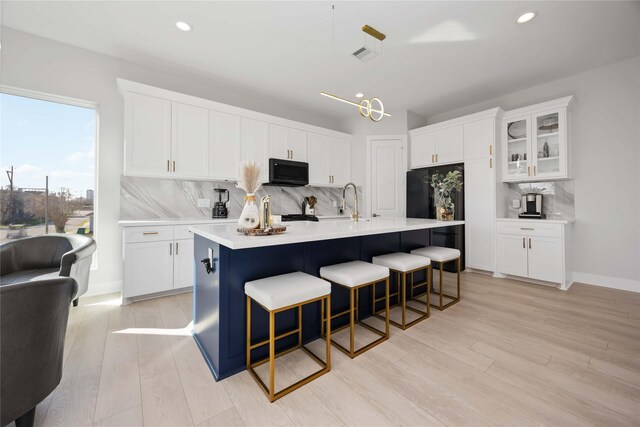 2422 Briley St, Houston, TX 77004 - kitchen featuring black microwave, a kitchen bar, backsplash, light countertops, and white cabinets