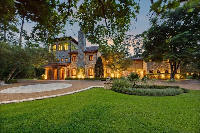603 W Friar Tuck Ln, Houston, TX 77024 - back of house at dusk with stone siding, a lawn, and a chimney