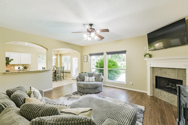 227 Fairwind Trail Dr, The Woodlands, TX 77385 - living area with arched walkways, ceiling fan, wood finished floors, and a tile fireplace