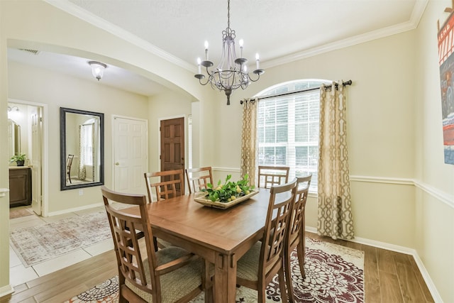 227 Fairwind Trail Dr, The Woodlands, TX 77385 - dining room with arched walkways, light wood-style flooring, a chandelier, and crown molding