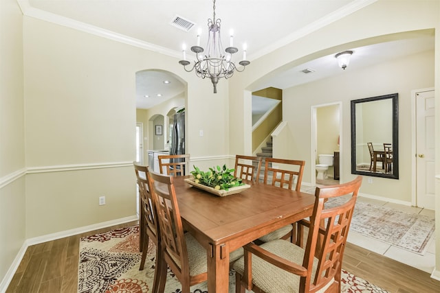 227 Fairwind Trail Dr, The Woodlands, TX 77385 - dining area with arched walkways, light wood-style flooring, stairway, a chandelier, and crown molding