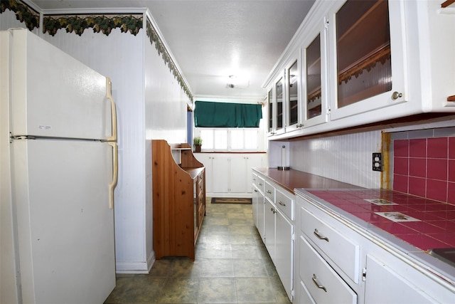 3614 Billingsley St, Houston, TX 77009 - kitchen featuring freestanding refrigerator, white cabinetry, tile countertops, decorative backsplash, and glass insert cabinets