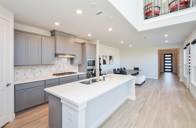 9522 Rialto Creek Dr, Cypress, TX 77433 - kitchen with gray cabinets, stainless steel appliances, light wood-style floors, tasteful backsplash, and a center island with sink