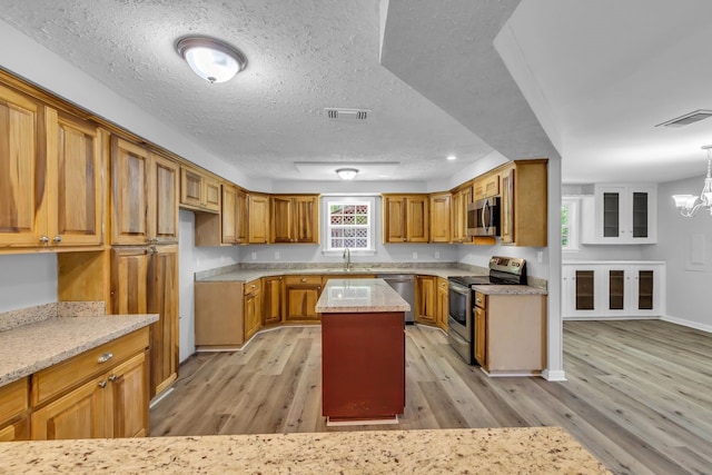 10650 Forest Creek Dr, Conroe, TX 77318 - kitchen with appliances with stainless steel finishes, light wood finished floors, brown cabinetry, a kitchen island, and a textured ceiling