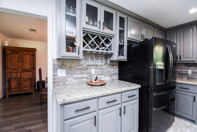 718 River Plantation Dr, Conroe, TX 77302 - kitchen with black fridge with ice dispenser, gray cabinetry, backsplash, glass insert cabinets, and light stone countertops