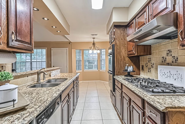 55 Sweetgum Ct, Lake Jackson, TX 77566 - kitchen with under cabinet range hood, appliances with stainless steel finishes, backsplash, light stone countertops, and hanging light fixtures