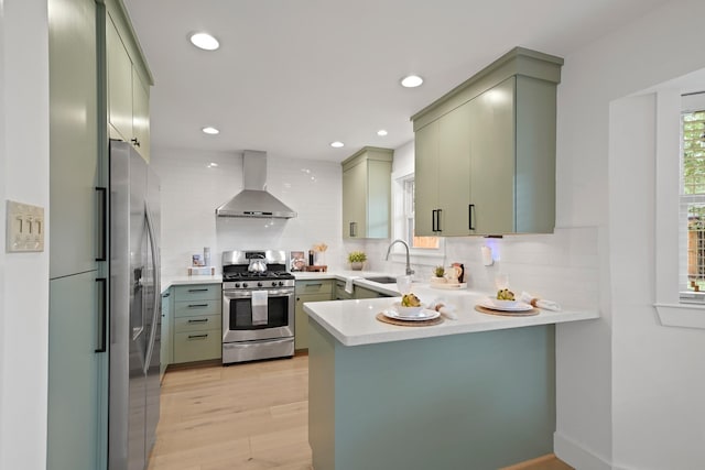 5730 Chrystell Ln, Houston, TX 77092 - kitchen with wall chimney range hood, appliances with stainless steel finishes, green cabinets, a peninsula, and backsplash