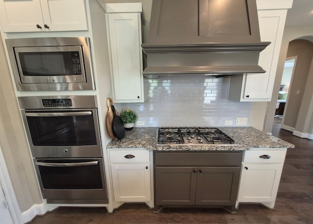7106 Prairie Grass Ln, Katy, TX 77493 - kitchen featuring appliances with stainless steel finishes, custom exhaust hood, arched walkways, decorative backsplash, and stone countertops