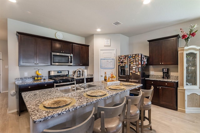 1614 Chase Anchor Ct, Richmond, TX 77469 - kitchen with appliances with stainless steel finishes, light wood-style flooring, dark brown cabinets, a kitchen breakfast bar, and recessed lighting