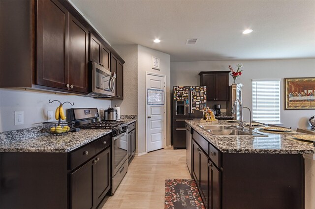 1614 Chase Anchor Ct, Richmond, TX 77469 - kitchen with appliances with stainless steel finishes, dark brown cabinets, light wood finished floors, a center island with sink, and stone countertops