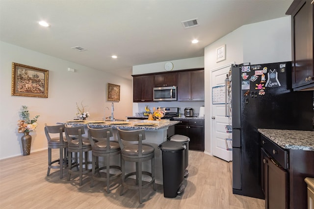 1614 Chase Anchor Ct, Richmond, TX 77469 - kitchen featuring appliances with stainless steel finishes, light wood finished floors, a kitchen bar, dark brown cabinetry, and a center island with sink
