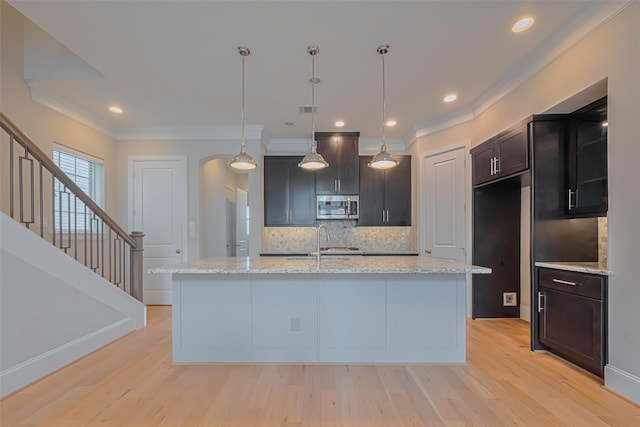8324 Ginger Oak St, Houston, TX 77055 - kitchen with stainless steel microwave, backsplash, light wood-style flooring, arched walkways, and ornamental molding