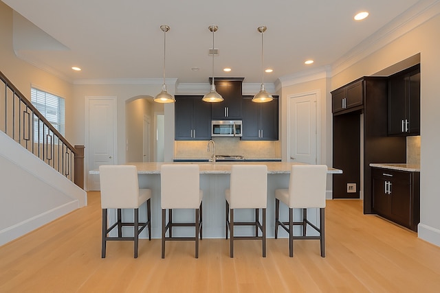 8324 Ginger Oak St, Houston, TX 77055 - kitchen featuring stainless steel microwave, light wood-style floors, tasteful backsplash, crown molding, and a kitchen bar